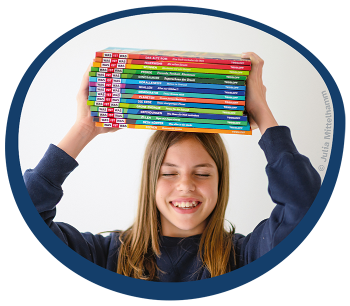 Lächelndes Kind mit WAS IST WAS Büchern auf dem Kopf