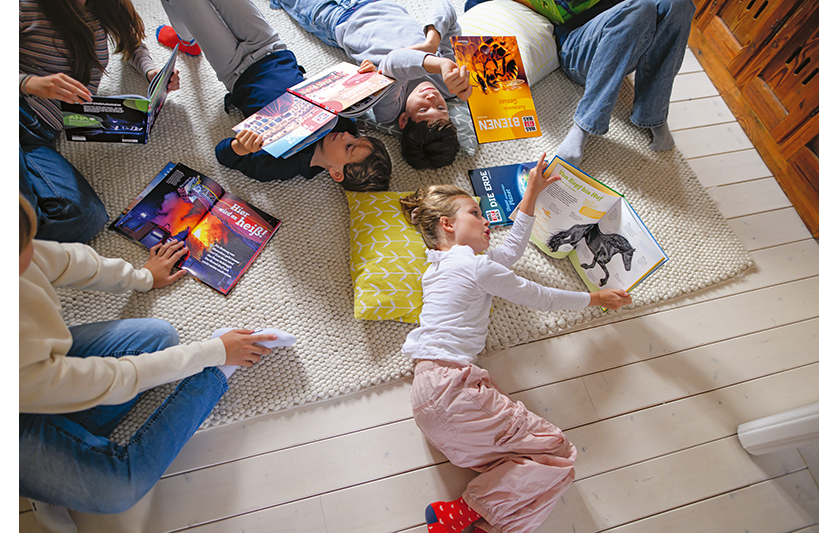 Eine Gruppe von Kindern liegt auf dem Boden und liest Was ist Was Bücher