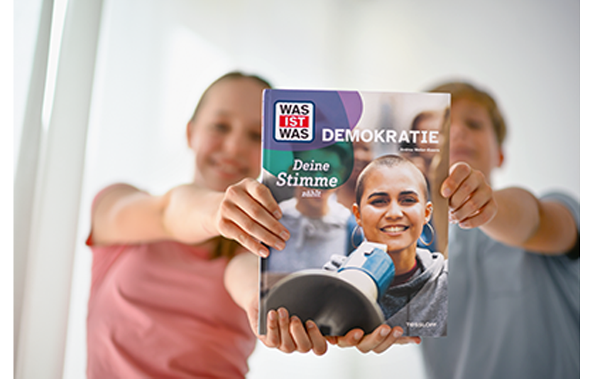 Zwei Kinder halten Buch Was ist Was Demokratie