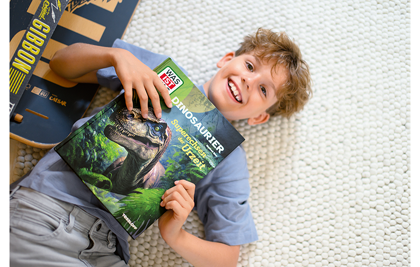 Junge hält Buch Was ist Was Dinosaurier