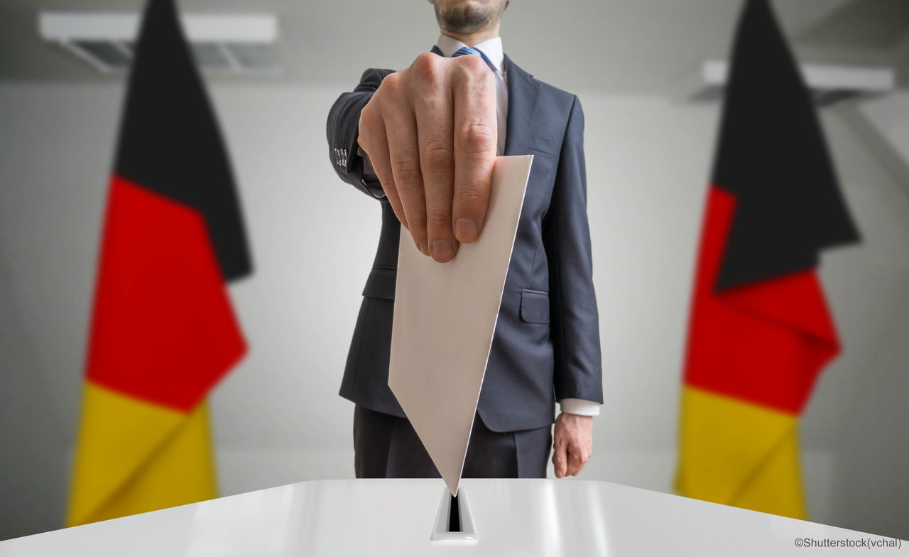Election or referendum in Germany. Voter holds envelope in hand above ballot. German flags in background.