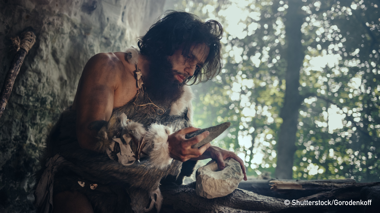 Primeval Caveman Wearing Animal Skin Holds Sharp Stone and Makes First Primitive Tool for Hunting Animal Prey, or to Handle Hides. Neanderthal Using Handax. Dawn of Human Civilization