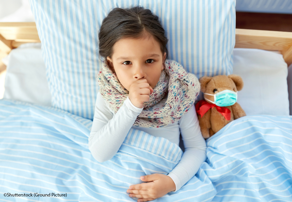 health, children and pandemic concept - sick coughing girl lying in bed with teddy bear toy wearing protective medical mask at home